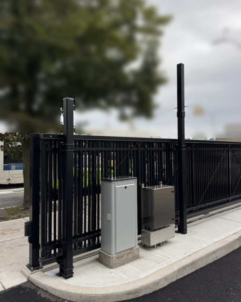 Black cantilever slide gate with a keypad pedestal at a vehicle entrance