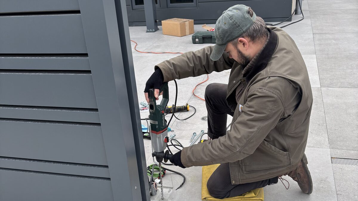 Fortis technician drilling a post anchor beside a new slat fence panel